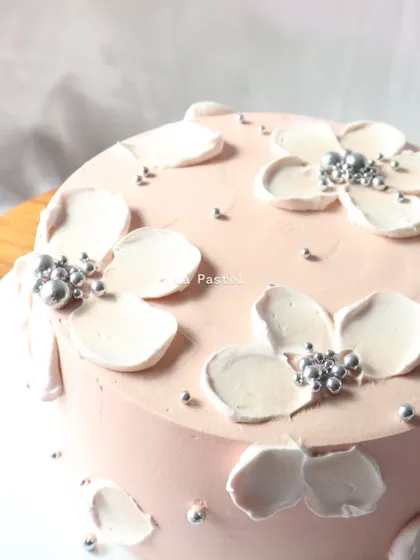 A pretty pink cake with white piped flowers and silver bead centers. A simple and lovely design.
