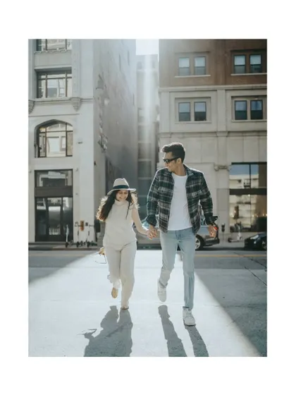 A candid shot of a couple running hand-in-hand down a sun-drenched Los Angeles street. The play of light and long shadows creates a dynamic, cinematic feel, capturing their joyful energy.