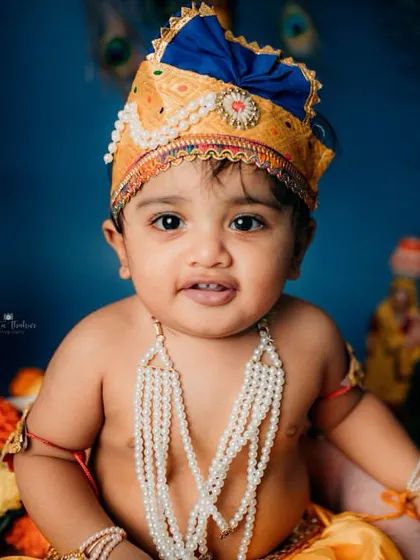 Looking straight at the camera with a gentle expression, this baby portrait showcases the beautiful details of the Krishna costume and the colorful studio setup.