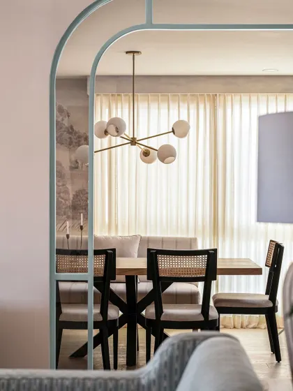 The dining room is framed by a beautiful duck egg blue partition, creating a soft yet moody atmosphere. The modern chandelier and cane-back chairs complete the modern coastal look.