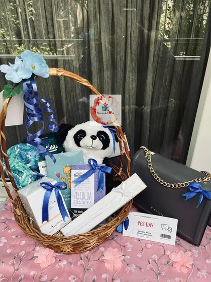 A full view of our panda-themed birthday basket, showcasing a handbag, chocolates, a soft toy, and other items all tied with beautiful blue ribbons.
