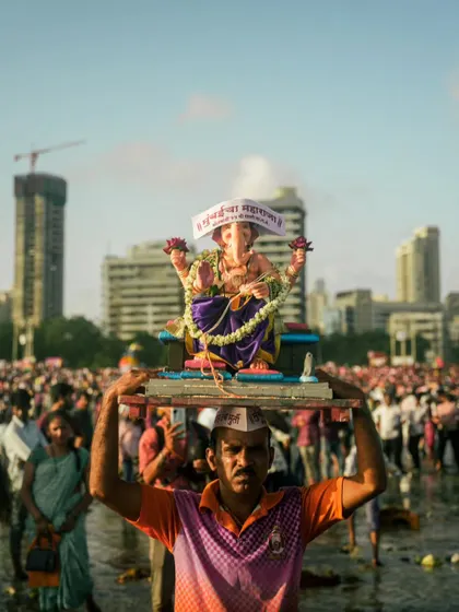 A devotee carries a household Ganesh idol on his head for immersion, surrounded by the massive crowd at Chowpatty. It shows the personal side of a festival known for its public grandeur.