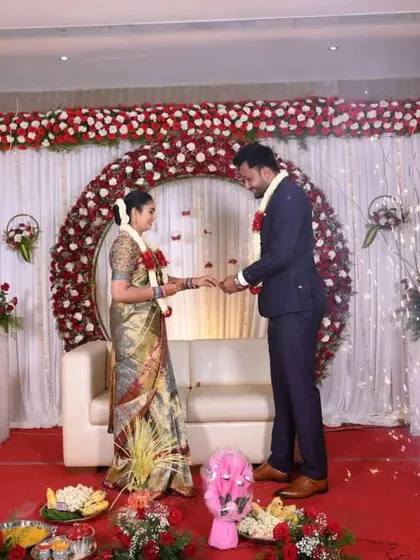 A couple exchanging rings during their engagement, set against a beautiful red and white rose arch.