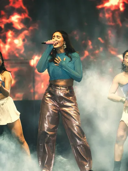 Fire and fashion. Dhvani performing on a smoky stage with dramatic fire effects, her colorful outfit standing out against the intense backdrop.