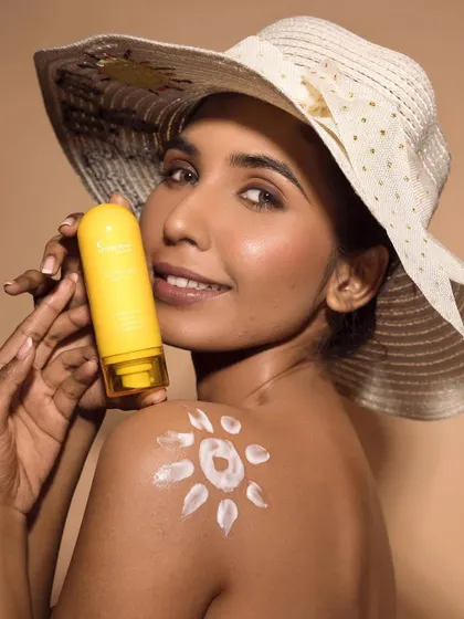 A creative and fun sunscreen campaign shot. The model wears a sun hat and has a sun drawn on her shoulder with sunscreen, visually communicating the product's purpose in a charming way. It’s a perfect image for summer campaigns, blending practicality with a touch of playfulness.