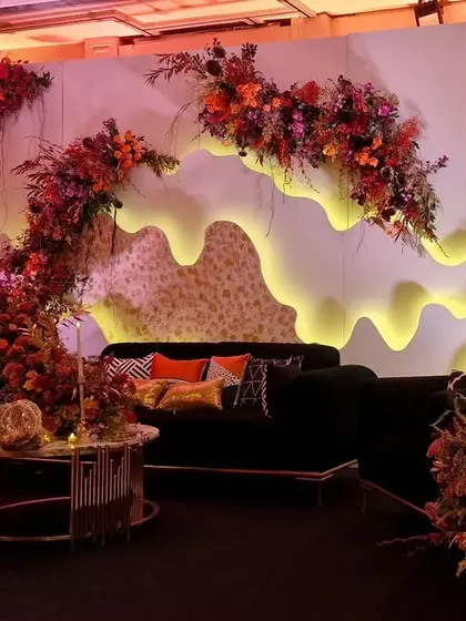 A unique stage and lounge area we designed with a custom-built, back-lit wavy backdrop. The dark sofas and cascading autumn-toned florals create a look that is both modern and warm.