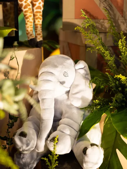 A soft, plush elephant toy sits among the greenery, adding a gentle and cuddly touch to the jungle-themed decorations.
