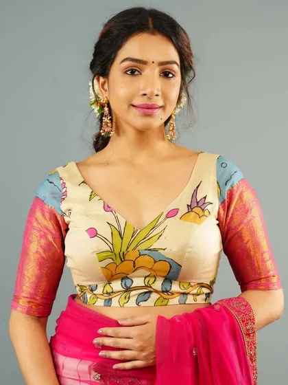 A V-neck blouse with a soft, hand-painted floral Kalamkari design. The contrasting pink sleeves with a gold border add a touch of brightness to the piece.