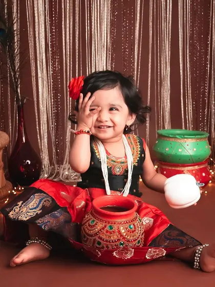A shy smile from this little darling. The traditional attire and festive props create a beautiful setting to celebrate cultural heritage in a milestone photoshoot.