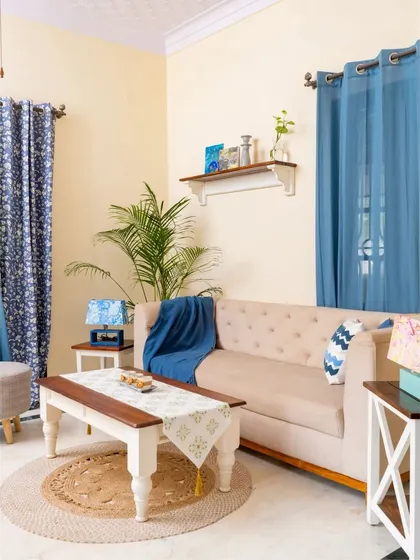 A complete view of a living room setting that blends farmhouse charm with Indian eclectic style. The space is tied together with a color palette of beige, blue, and wood tones, creating a cozy and inviting atmosphere.