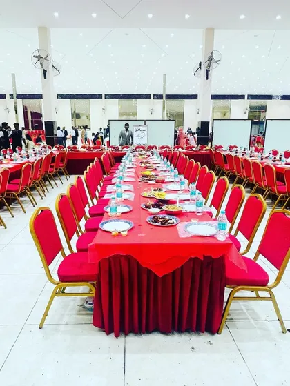 A wide shot of the dining hall at a wedding function. The vibrant red chairs and tables create a festive look, all set up by our team.
