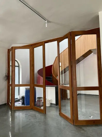 A folding glass and wood partition provides flexibility, allowing spaces to be opened up or closed off while reflecting the spiral staircase beyond.