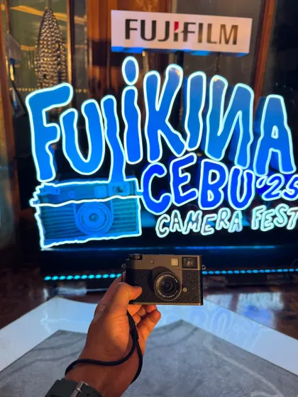 A close-up of the Fujifilm X half camera against the neon sign of the Fujikina event. This is a creative product shot that highlights the camera as the star of the show.