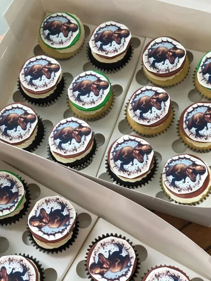A box of dinosaur-themed cupcakes, perfect to accompany a Jurassic Park or dinosaur birthday cake.