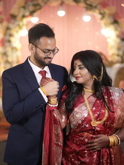 The groom holds his bride's hand, a gesture of reassurance and love. This portrait from a Bengali wedding captures the couple's connection amidst the celebration.