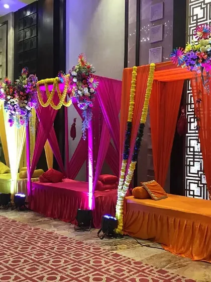 A vibrant Mehendi setup with colorful shamiyana-style seating areas in shades of green, yellow, pink, and orange, each topped with a lush floral arrangement.