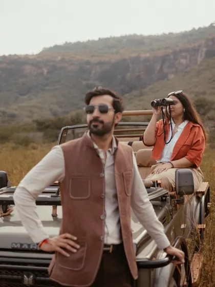 A stylish shot from a Ranthambore pre-wedding shoot, with the groom posing by the jeep while the bride looks on with binoculars.