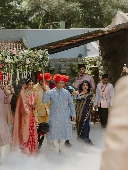 The bride makes her entrance under a 'phoolon ki chadar' (floral canopy), surrounded by smoke effects.