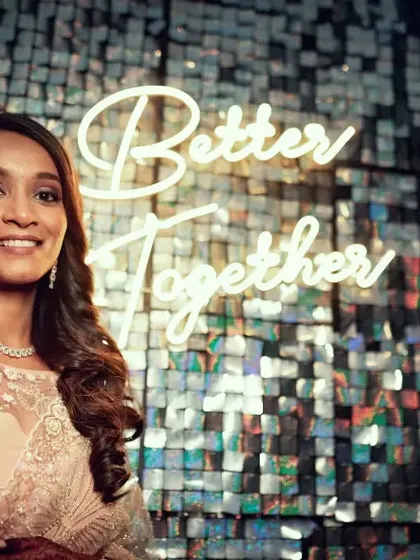 A beautiful portrait of the bride at her reception, standing in front of a "Better Together" neon sign and a sparkling backdrop.