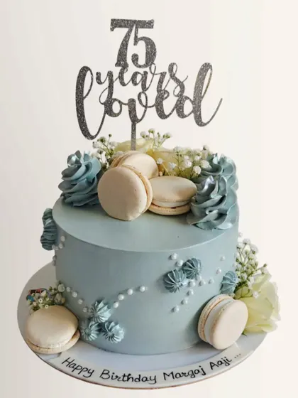 A lovely pastel blue cake for a 75th birthday, topped with macarons and delicate flowers. The "75 years loved" topper makes it extra special.