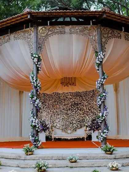 A stunning reception mandap, with a domed structure, elegant drapes, and a backdrop wall completely covered in flowers.