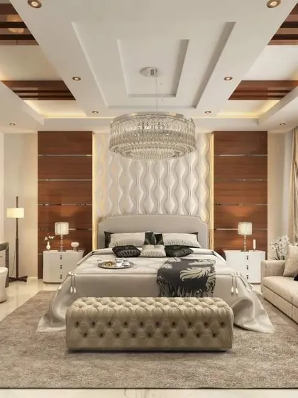 This grand master bedroom features a custom bed with a textured headboard and an integrated vanity table. The complex false ceiling with a crystal chandelier adds to the luxurious feel.
