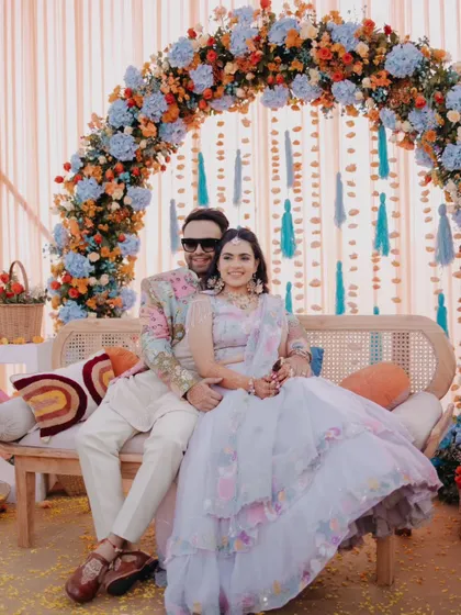 A classic portrait of the couple seated under their colorful Haldi decor, smiling for the camera.