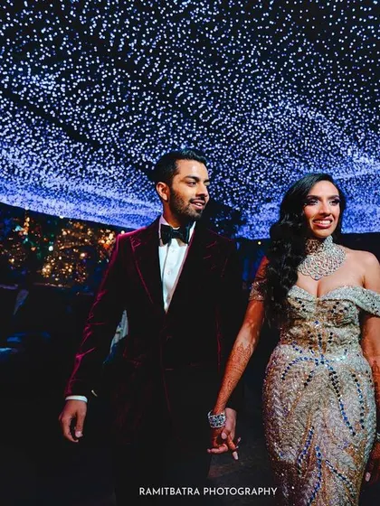 The couple walks hand-in-hand under a ceiling of twinkling fairy lights, creating a magical, starry night effect.