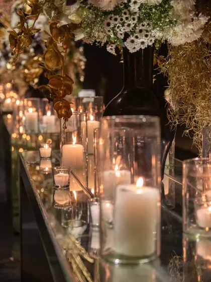 The warm light from the candles catches the texture of the flowers and the reflective surfaces of the table. This image captures the intimate and luxurious ambiance we create through careful lighting and material choices.
