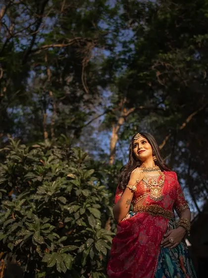A low-angle shot of the bride standing tall and confident amongst the trees. The sunlight filtering through the branches creates a majestic, natural spotlight.