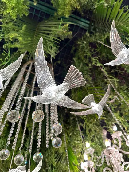A close-up of the crystal bird figures and hanging crystals amidst the greenery of the whimsical wild ceiling, showcasing the mesmerizing details.