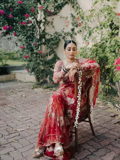 A portrait of the bride seated in a garden, her expression calm and poised. The beautiful floral Sabyasachi saree and the natural setting combine to create an image of timeless elegance.