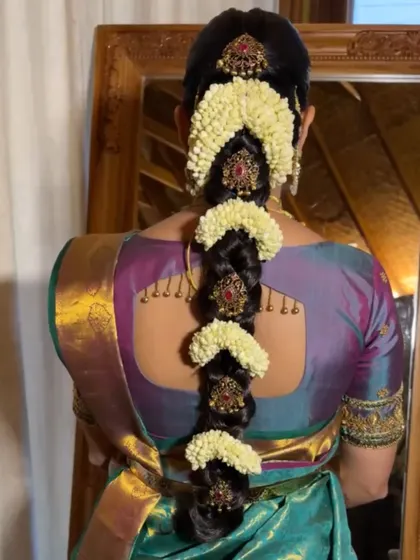A still image capturing the intricate details of a floral and jeweled bridal braid. The combination of fresh malli poo and gold accessories is a hallmark of the muhurtham look.