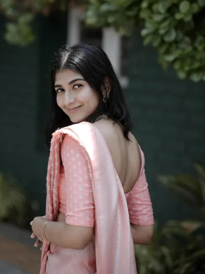A classic and graceful over-the-shoulder pose. The soft light and natural green background complement her pink saree, creating a timeless and elegant portrait.