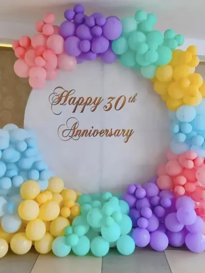 A soft and cheerful 30th anniversary celebration, featuring a circular backdrop framed with a rainbow of pastel balloons.