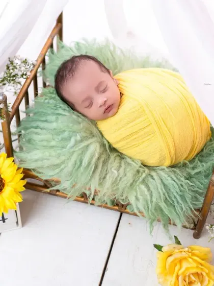 A sweet newborn swaddled in sunny yellow, resting on a miniature bed surrounded by sunflowers. This bright and cheerful setup is perfect for a summer baby.