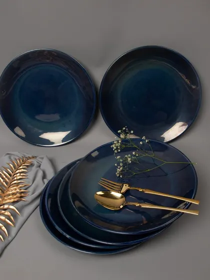 An elegant tabletop arrangement of deep blue ceramic dinner plates, styled with golden cutlery and delicate flowers to create a sophisticated dining aesthetic.