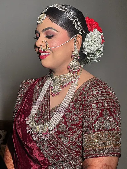 A happy bride in a stunning maroon velvet lehenga. The look is completed with a beautiful floral bun and a radiant smile.