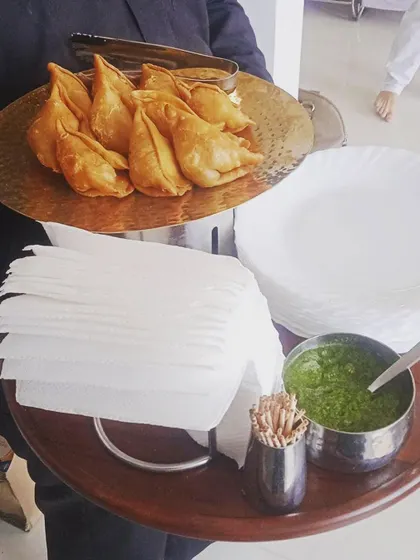 A tray of freshly fried samosas being served as part of a pure vegetarian menu for a Hawan ceremony.
