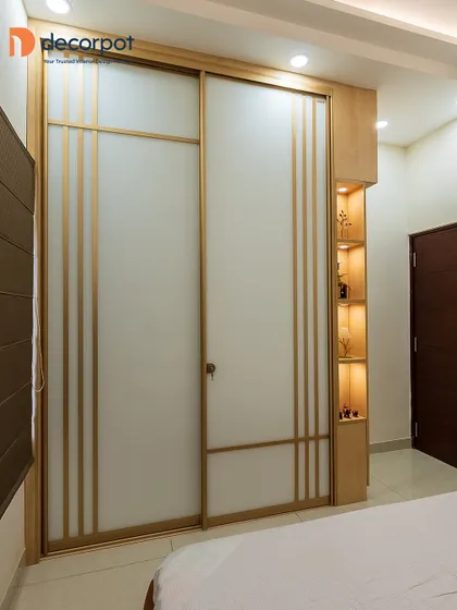 A sliding wardrobe with elegant gold-colored inlay details and integrated open shelving. The warm backlighting in the shelves provides a perfect spot for displaying decor, making the wardrobe a multi-functional piece.
