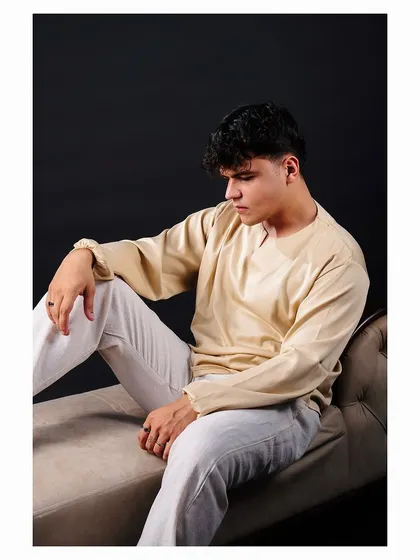 A studio portrait of a model in a cream-colored kurta and white pants. The lighting is soft, highlighting the texture of the fabric, making it ideal for showcasing men's ethnic or resort wear.