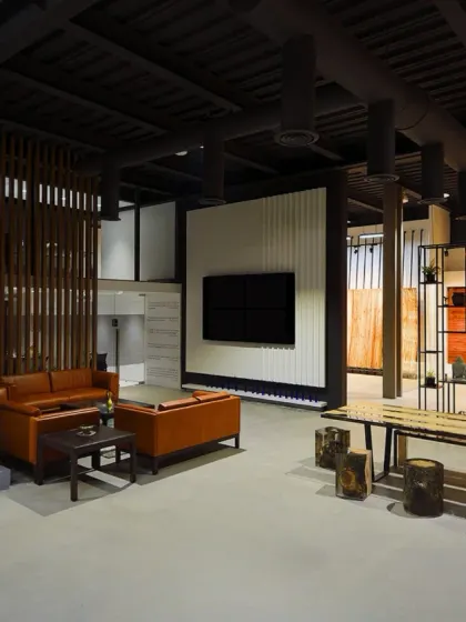 A lounge area within the showroom, featuring a mix of rustic and modern furniture. The space is defined by wooden partitions and a large media screen, creating a comfortable spot for client consultations.