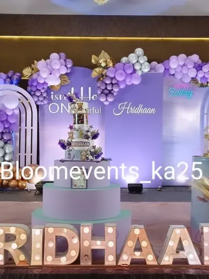 A sophisticated birthday stage in shades of purple and gold. The decor includes arched backdrops, a lush balloon garland, and personalized light-up marquee letters for the birthday boy.