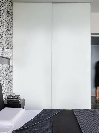 A wider view of the guest room in 'A Wedged Haus', showing how the white back-painted glass wardrobe doors contrast with the textured terrazzo wall. The design uses large, simple planes of material to define the space.