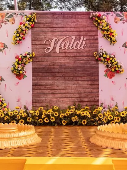 The main stage for a Haldi ceremony, featuring a rustic wooden backdrop adorned with sunflowers. This design combines natural elements with bright florals for a warm and inviting feel.