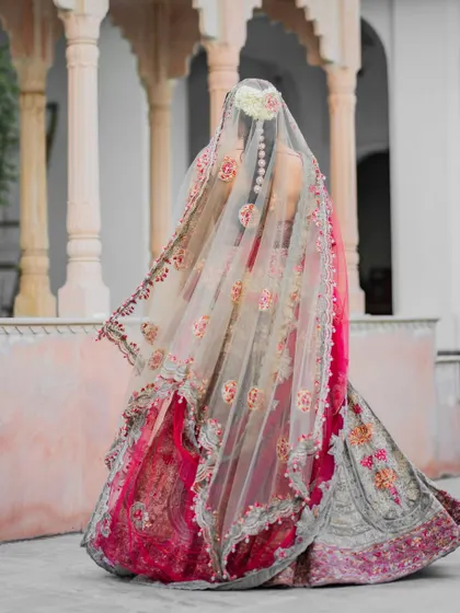 A back profile of the bride, focusing on the exquisite details of her embroidered veil and the floral arrangement in her hair. This shot emphasizes the artistry of the bridal attire.