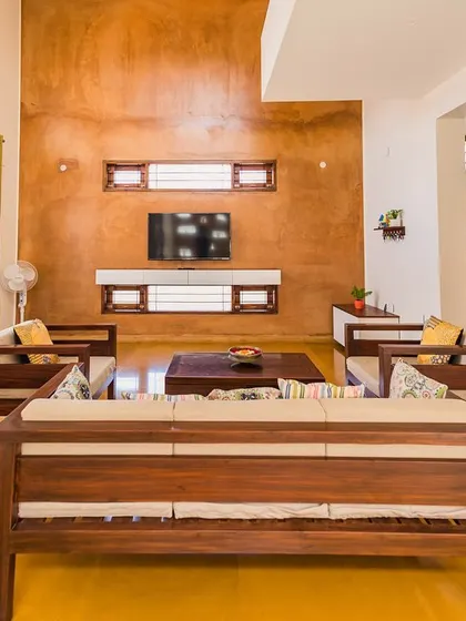 The living room in Anand and Madhu's home features a stunning rammed earth wall as the backdrop. The space is designed to be warm and inviting, with custom wooden furniture and large openings to the outside.