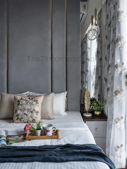 A detail shot of the master bedroom styling. The embroidered floral cushion adds a soft, decorative touch against the structured, paneled headboard, showcasing a blend of textures.