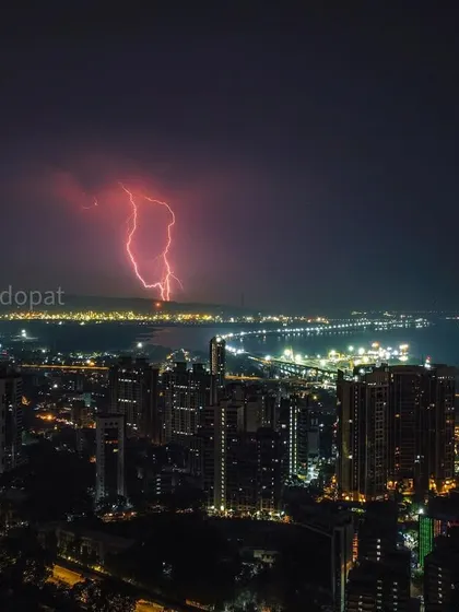A dramatic display of power as red lightning strikes across the sea, illuminating the Mumbai skyline. Capturing storms requires patience and readiness to photograph these fleeting, intense moments of nature's force.