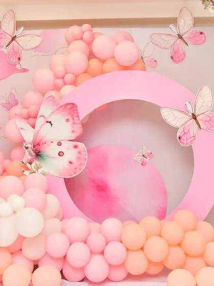 A circular panel with a large butterfly cutout, surrounded by a garland of pink and orange balloons.